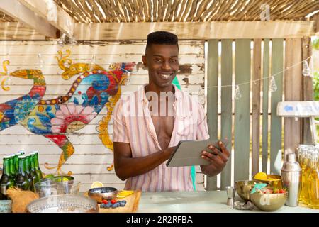 Ritratto di barista afro-americano con tavoletta in spiaggia, inalterato Foto Stock