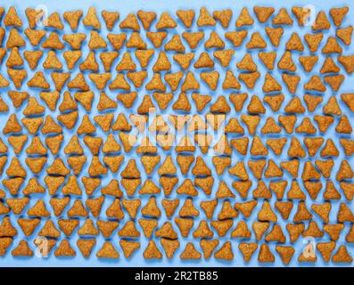 Divertente giacitura piatta di ciottoli da compagnia disposti su uno sfondo blu. Palline a forma di triangolo di alimenti secchi per cani o gatti vista dall'alto Foto Stock