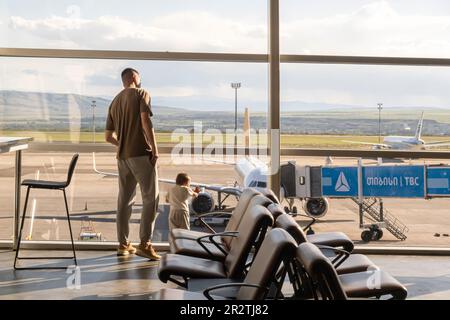 Area d'attesa dell'Aeroporto Internazionale di Tbilisi, padre e bambino che guardano il campo aereo attraverso la finestra TBS, Tbilisi, Georgia Foto Stock