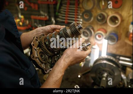 Servizio di riparazione motociclette al coperto con primo piano sulle mani del tecnico addetto alla manutenzione che tengono l'ingranaggio Foto Stock