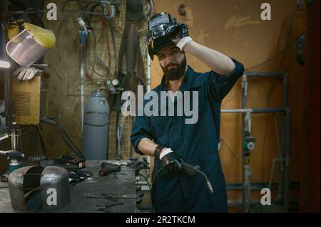 Ritratto del riparatore che tacca il casco protettivo dopo un duro lavoro con la saldatrice Foto Stock