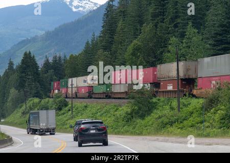 BC, Canada-Agosto 2022; Vista lungo il terrapieno ferroviario lungo la Trans-Canada Highway con locomotive canadesi del Pacifico che tirano le auto con container Foto Stock