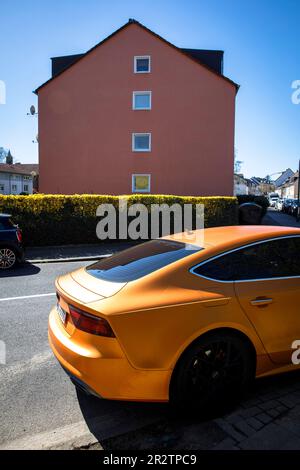 Una Audi A5 Sportback arancione è parcheggiata di fronte ad una casa rossa nel quartiere Niehl di Colonia, in Germania. ein orangefarbener Audi A5 Sportback steht vo Foto Stock