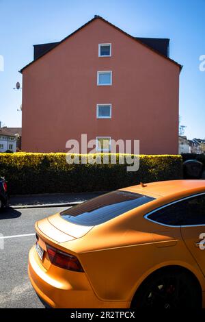 Una Audi A5 Sportback arancione è parcheggiata di fronte ad una casa rossa nel quartiere Niehl di Colonia, in Germania. ein orangefarbener Audi A5 Sportback steht vo Foto Stock