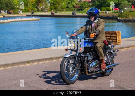 Poole, Dorset, Regno Unito. 21 maggio 2023 Bournemouth and Poole Distinguished Gentlemen's Ride è un evento annuale, uno dei tanti in tutto il mondo, per raccogliere fondi e sensibilizzare sulla salute degli uomini. Durante il loro viaggio, centinaia di moto, molte vintage, attraversano Poole Park sulla strada per Bournemouth con molti dei loro piloti vestiti in modo appropriato, in stile retrò cravatte, baffi e tweeds in una bella giornata di sole. Uomo vestito con giacca e cravat in moto Triumph con cestino da picnic sul retro Credit: Carolyn Jenkins/Alamy Live News Foto Stock