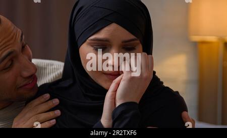 L'uomo afroamericano si preoccupa di triste offeso piangere la donna musulmana araba coppia multirazziale diversa siede indoor amoroso marito calmante moglie cocdling Foto Stock