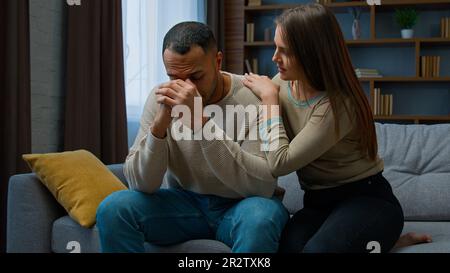 Disperato uomo triste sedersi sul divano sconvolto con cattive notizie lamentare la vita problema cura moglie sostegno ragazzo. Scusante donna dire scusa abbracciare infastidito Foto Stock