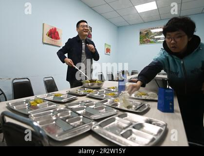 (230521) -- SHENYANG, 21 maggio 2023 (Xinhua) -- Zhao Qiang (L) prepara il cibo per gli intellettualmente sfidati a Shenyang, provincia di Liaoning della Cina nord-orientale, 18 aprile 2023. Quando Zhao Qiang aveva due anni, sviluppò una malattia che gradualmente risultò una disparità di 23 centimetri tra due gambe. Fissò uno sgabello sulla suola del piede sinistro su suggerimento della sua famiglia e si adattò a camminare con esso. Zhao Qiang ha dovuto abbandonare presto a causa della malattia, ma dopo un duro lavoro, è stato ammesso alla Northeastern University, laureandosi in computer per l'istruzione continua. Zhao Qiang ha Foto Stock