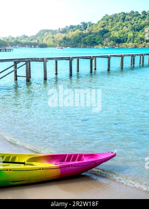 Vuoto colorato kayak con nessuno sulla spiaggia di sabbia pulita vicino al ponte di legno su sfondo blu mare, stile verticale, attività attrezzature preparano per re Foto Stock