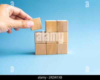 Ultimo pezzo di legno blocco cubo in mano mettendo su puzzle di legno impilamento disposizione compleated isolato su sfondo blu, stile minimal. Soluzione, risolvere Foto Stock