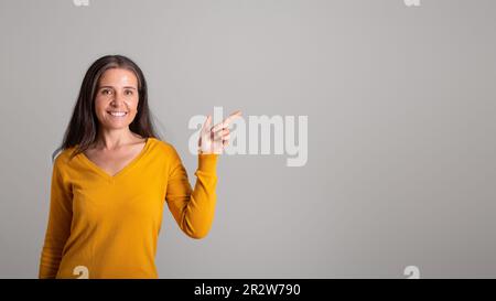 Donna di età caucasica positiva puntando il dito sullo spazio libero, raccomandando la vendita Foto Stock