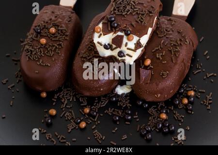 Gelato fuso e morso con bastoncini di legno, cacao con caramelle decorative sulla superficie nera Foto Stock