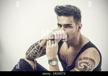 Bel giovane tatuato che indossa una t-shirt grigia, in piedi Foto Stock