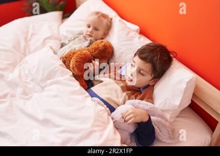 Adorabile ragazzo e ragazza che abbraccia orsacchiotto che dorme a letto in camera da letto Foto Stock