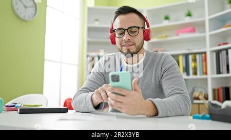 Studente ispanico che utilizza lo smartphone indossando le cuffie presso la biblioteca universitaria Foto Stock