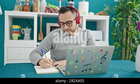 Uomo ispanico che indossa le cuffie utilizzando la scrittura sul notebook in sala da pranzo Foto Stock