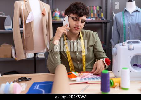 Non binary man Tailor Talking su smartphone cercando colore test presso atelier Foto Stock