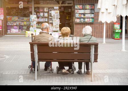 Tre persone anziane con accessori per ausili alla mobilità seduti su una panca pubblica. Spazio di copia vuoto per il testo dell'editor. Foto Stock
