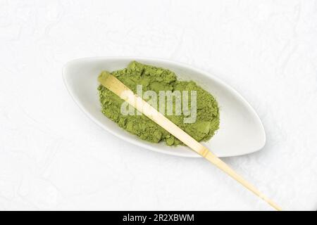 Misurino di bambù in una ciotola con polvere di matcha. Giacitura piatta. Sfondo bianco Foto Stock