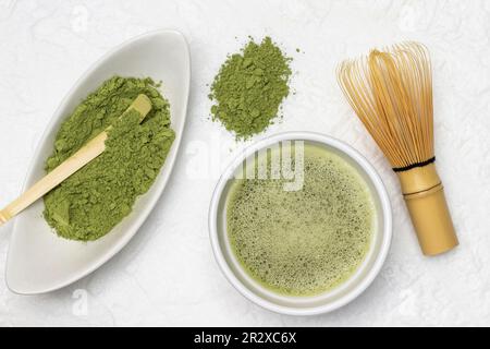 Cucchiaio di bambù in una ciotola di polvere di matcha. Tè verde Matcha in una ciotola. Frusta di bambù sul tavolo. Giacitura piatta. Sfondo bianco Foto Stock