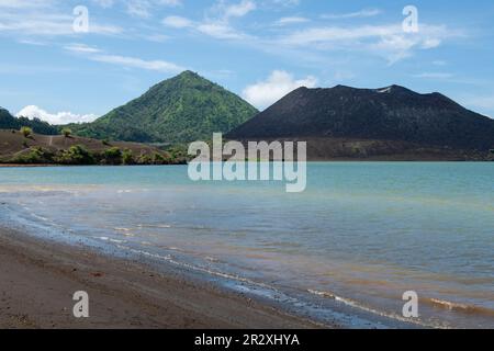 Papua Nuova Guinea, Isola della Nuova Gran Bretagna, Rabaul, sorgenti termali. Spiaggia di sabbia nera con il vulcano Tavurvur in lontananza. Foto Stock