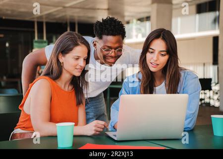 Gruppo di studenti adolescenti multirazziali felici che utilizzano il laptop, lavorando al progetto di compiti universitari in biblioteca universitaria. Incontro di giovani diversi alla ricerca di informazioni sul computer. Foto di alta qualità Foto Stock