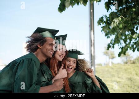 Tre amici scattano una foto per celebrare la loro laurea con la tuta di confine. Concetto: Laurea, università, studi Foto Stock