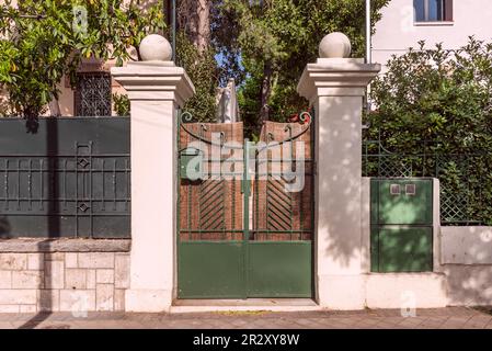 Portale di una casa unifamiliare urbana con recinzione metallica con opere in ferro battuto dipinto di verde scuro abbinate a pietra, siepi e alberi Foto Stock