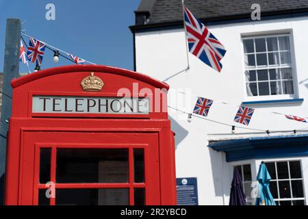 Scatola telefonica rossa britannica con un tipico pub britannico sullo sfondo e bandiere Union Jack, bunting Foto Stock