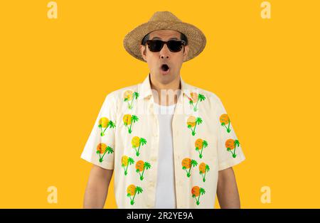 Uomo latino in vacanza indossando camicia floreale cappello occhiali da sole su sfondo giallo isolato paura e scioccato con sorpresa espressione, paura e eccitazione Foto Stock