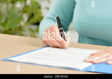 Primo piano immagine frontale di una mano che firma un contratto su un desktop in ufficio Foto Stock