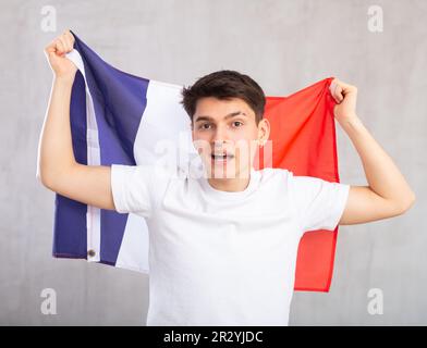 Eccitato, attivo spettatore maschile detiene bandiera nazionale della Francia in mani e canti slogan popolare Foto Stock