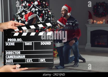 Ripresa di un filmato. Seconda macchina fotografica assistente che tiene il clapperboard di fronte alla felice famiglia che celebra il Natale (attori) a casa (set cinematografico) Foto Stock