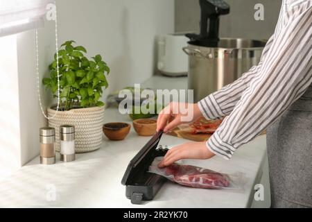 Donna che usa il sigillante per il confezionamento sottovuoto in cucina, closeup. Cucina sous vide Foto Stock