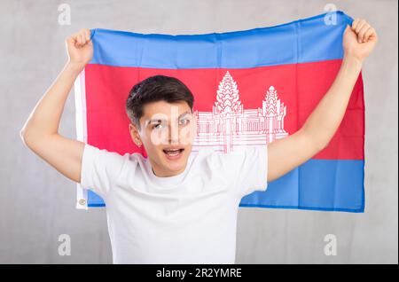 Eccitato, attivo spettatore maschile tiene bandiera nazionale della Cambogia in mani e canti slogan popolare. Foto Stock