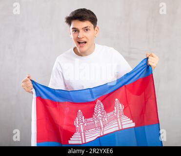 Eccitato, attivo spettatore maschile tiene bandiera nazionale della Cambogia in mani e canti slogan popolare. Foto Stock