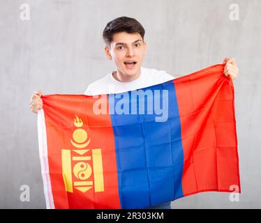 Eccitato, attivo spettatore maschile tiene bandiera nazionale della Mongolia in mani e canti slogan Foto Stock