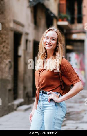 Ritratto verticale di un giovane turista caucasico nelle strade del centro storico di Barcellona. Sta posando per la macchina fotografica e sorridendo Foto Stock