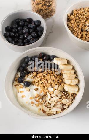 Granola fatta in casa con yogurt greco, mandorle, mirtilli e banana in una ciotola. Foto Stock