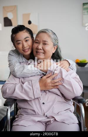 Nonna in visita nonna in casa di cura e abbracciarla da dietro per esprimere l'amore Foto Stock