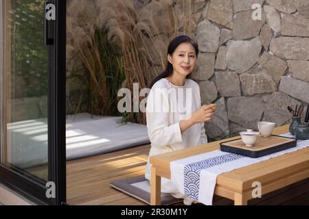 Elegante donna cinese matura che beve il tè in sala da tè Foto Stock