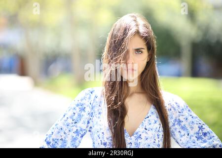 Donna arrabbiata con i capelli tousled una giornata ventosa guardando la macchina fotografica in strada Foto Stock