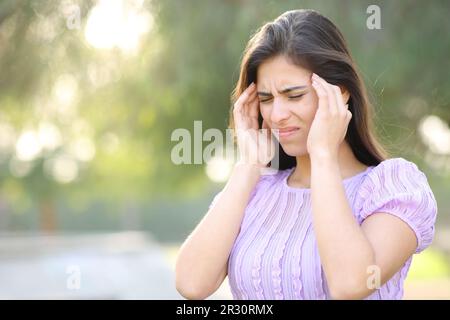 Donna che soffre di emicrania a piedi in un parco Foto Stock