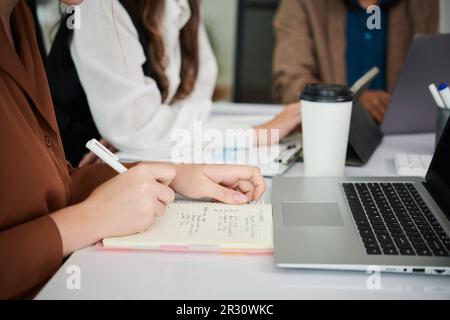 Donna d'affari seduta al tavolo dell'ufficio con i colleghi, bere caffè e prendere appunti in pianificatore Foto Stock