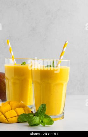 Frullato di mango giallo fresco in bicchieri con paglia, frutta fresca e menta. Orientamento verticale Foto Stock