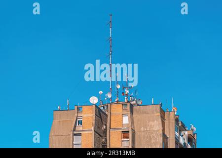 Antenne di comunicazione e parabole satellitari in cima ad un alto edificio residenziale con cielo blu sullo sfondo Foto Stock