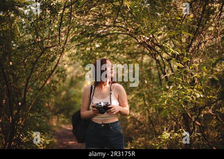 Donna turistica che tiene la macchina fotografica mentre si trova in piedi nella foresta durante l'estate Foto Stock