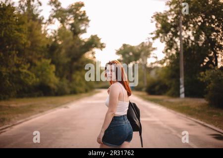 Giovane donna che cammina sulla strada di campagna durante l'estate Foto Stock