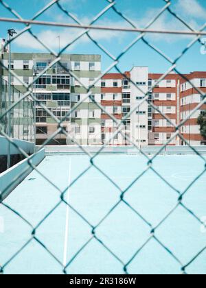 Campo da calcio blu attraverso recinzione con edifici sullo sfondo Foto Stock