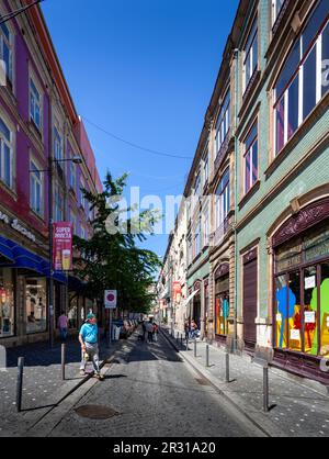 Uomo che cammina lungo la strada acciottolata della città vecchia di Porto con edifici rivestiti di piastrelle su entrambi i lati. Giorno luminoso e soleggiato con il cielo limpido portoghese. Foto Stock